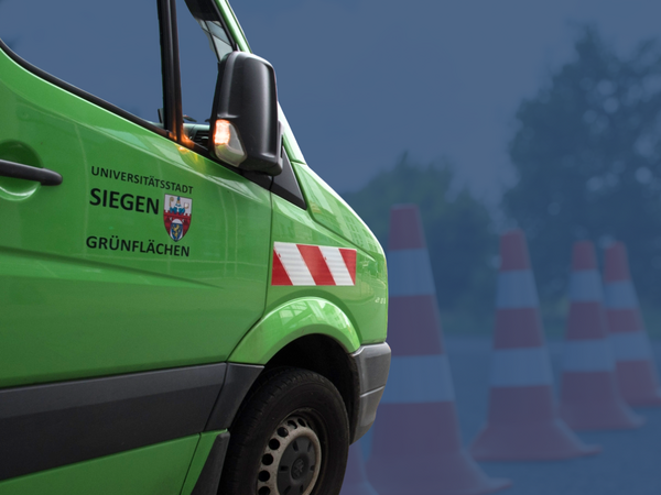 Links ein grünes Auto der Grünflächenabteilungen der Stadt Siegen, im Hintergrund Leitkegel