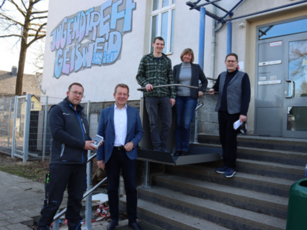 Der neue Außenlift im Kinder- und Jugendtreff Geisweid überwindet die Stufen bis zum Eingang. Bürgermeister Steffen Mues (2.v.l.) und Mitarbeitende der Stadt Siegen wie der Fachfirma bei der ersten „Probefahrt“. (Foto: Stadt Siegen)