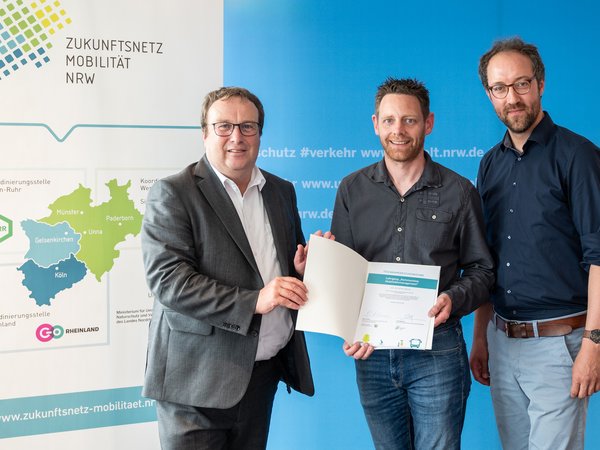 Bei der Übergabe der Urkunde (v.l.): NRW-Verkehrsminister Oliver Krischer, Jan König und Christoph Overs, Geschäftsstellenleiter Zukunftsnetz Mobilität NRW (Foto: Ministerium für Verkehr NRW/Caroline Seidel)