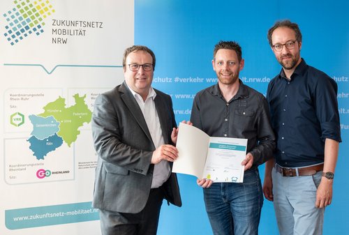 Bei der Übergabe der Urkunde (v.l.): NRW-Verkehrsminister Oliver Krischer, Jan König und Christoph Overs, Geschäftsstellenleiter Zukunftsnetz Mobilität NRW (Foto: Ministerium für Verkehr NRW/Caroline Seidel)