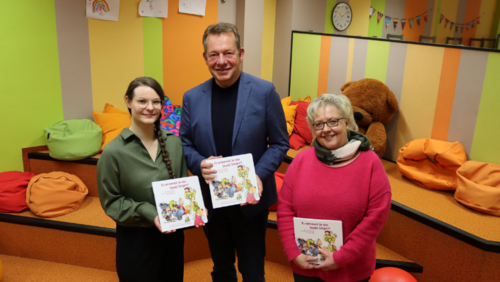 Die stellv. Leiterin der Stadtbibliothek, Dana Jaschke (l.) und Bürgermeister Steffen Mues (Mitte) freuen sich über den Neuzugang in der Kinderecke, das Siegener Wimmelbuch, gestaltet von Illustratorin Kathrin Klotzki-Progri (r.). (Foto: Stadt Siegen)