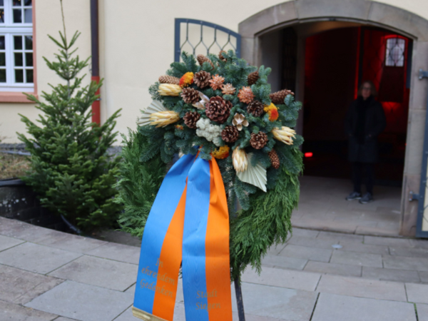 Das Bild zeigt einen Gedenkkranz (auch Trauerkranz genannt), der vor der 'Gedenkstätte für die Opfer des Krieges und der Gewalt', am Dicken Turm des Unteren Schlosses aufgestellt ist.