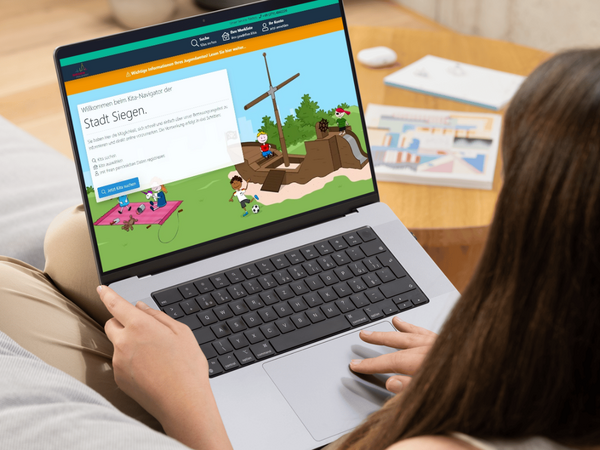 Auf dem Bildschirm ist der Kita-Navigator der Stadt Siegen abgebildet, ein Online-Portal zur Suche und Vormerkung von Betreuungsplätzen in Kindertageseinrichtungen (Kitas) und in der Tagespflege. 